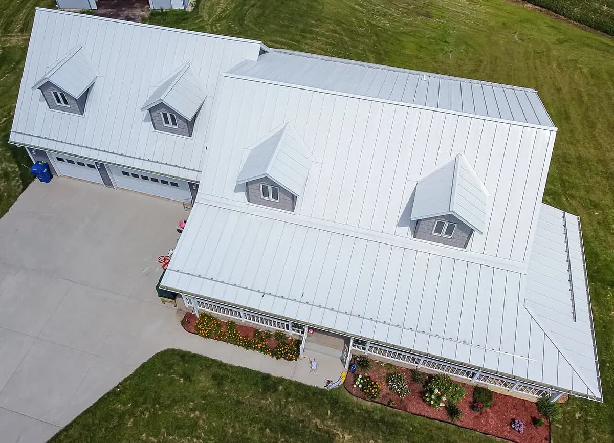 Aerial view of a house with a white standing-seam metal roof and several dormers.